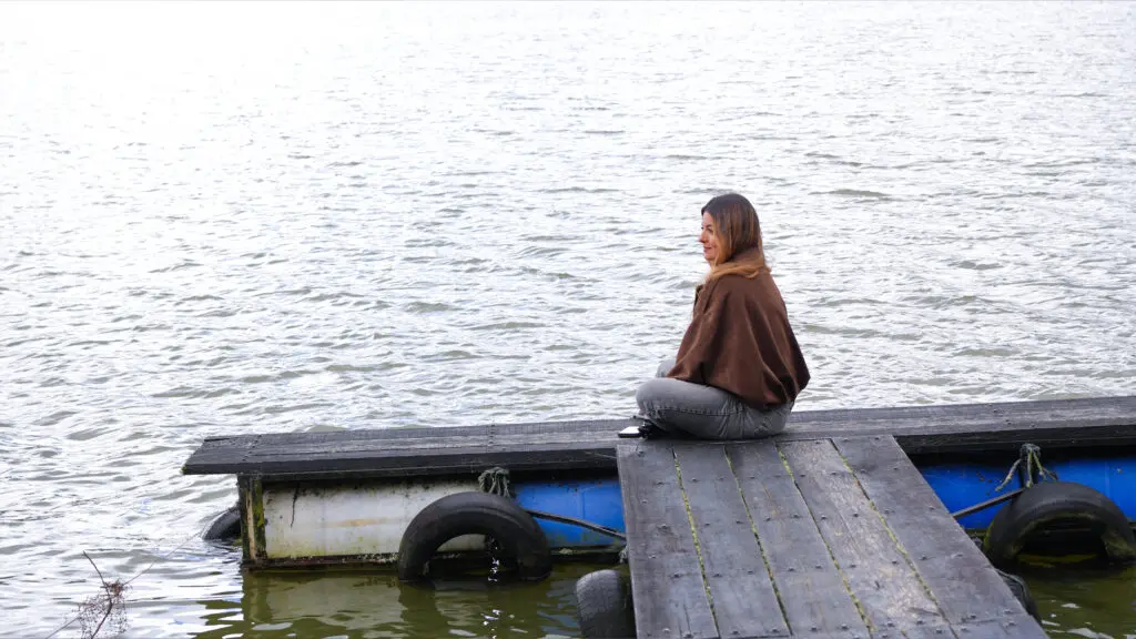Mujer rubia joven sentada en un muelle, embalse del sisga