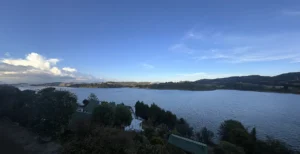 Laguna del sisga con cielo azul, montañas de fondo y arboles