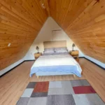 Cama doble con edredón de líneas azules, mesas de noche de madera clara y lámparas de mesa rústicas